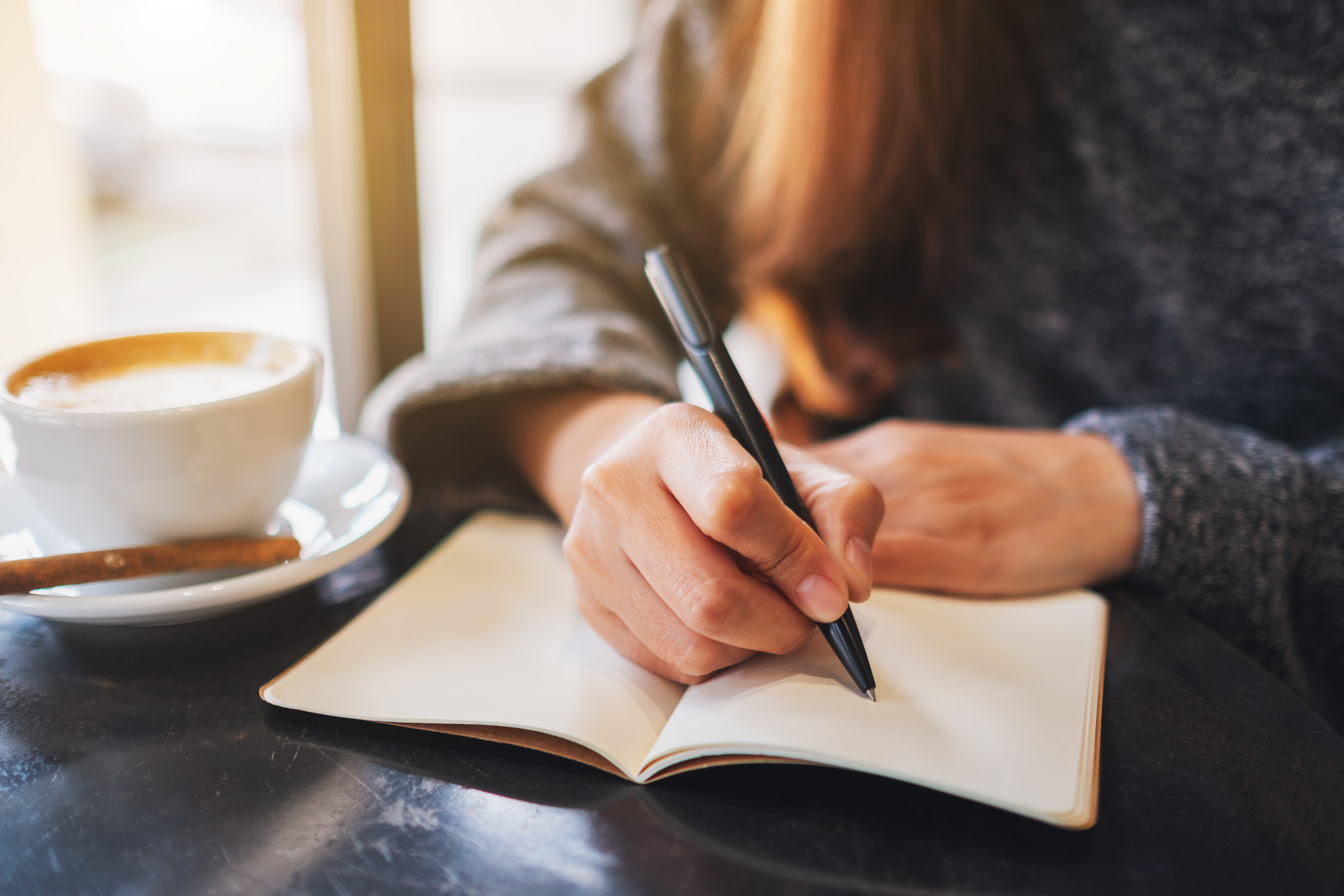 Person with a coffee writing in a notebook