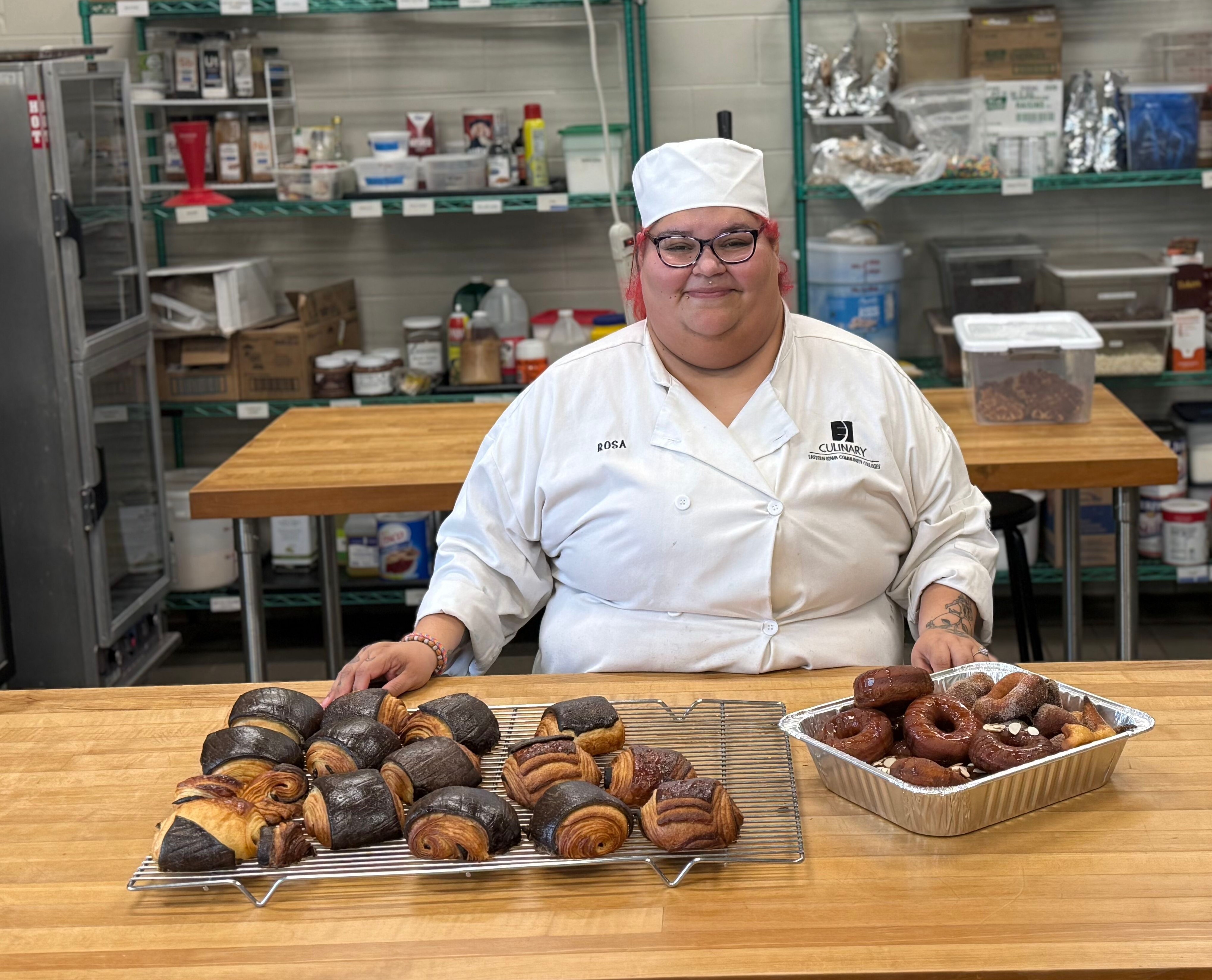 Rosamarie Gomez stands next to a table holding the baked goods she made in class. 