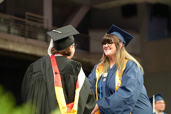 Joeanna Moore smiles as she shakes hands with SCC President Ann Lawler in academic regalia while receiving her diploma on stage during graduation.