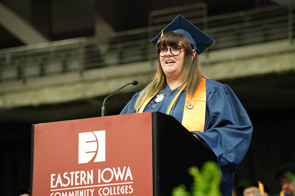  Joeanna Moore, dressed in a navy graduation cap and gown with gold honors stole, speaks at the podium during the Eastern Iowa Community Colleges commencement ceremony.